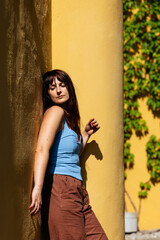 Fototapeta premium Young caucasian female relaxing in sunlight near vibrant yellow wall