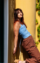 Fototapeta premium Young caucasian female leaning on yellow wall in sunlight