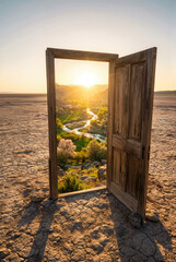 Open wooden door in cracked desert, sunrise over green river valley, concept of return to freedom, new beginning, migration, hope, journey to free country.