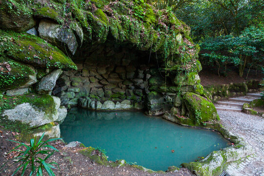 A tranquil, turquoise pool is nestled within a grotto of moss-covered rocks