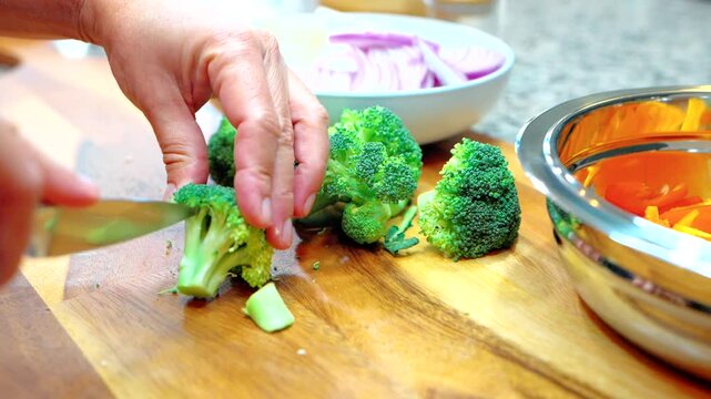 chef chopping fresh broccoli florets on a wooden cutting board