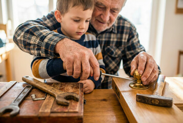 Senior man and young boy repairing metal door handle with screwdriver on wooden work surface.