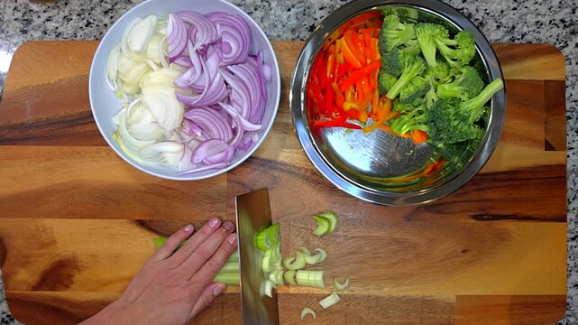 close up of hands slicing fresh celery on wooden board with various vegetables