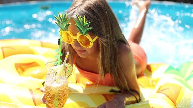 little girl swimming in a pool in the summer on a mattress with a cocktail and sunglasses