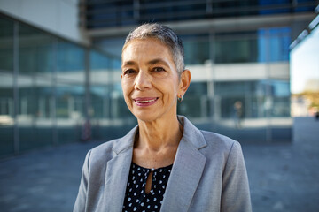 Confident senior businesswoman smiling outside modern office