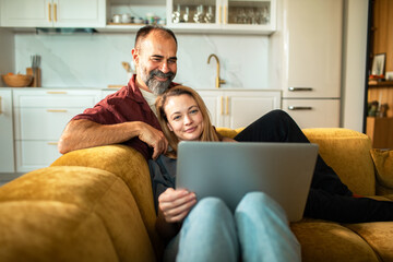 Happy couple relaxing with laptop on sofa at home