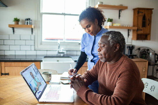Senior man and caregiver during telehealth consultation in home kitchen