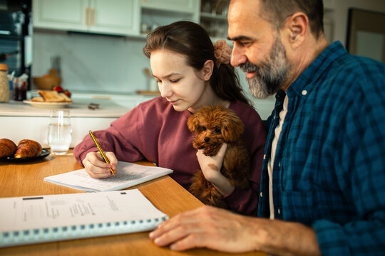 Father helping daughter with homework at kitchen table with puppy