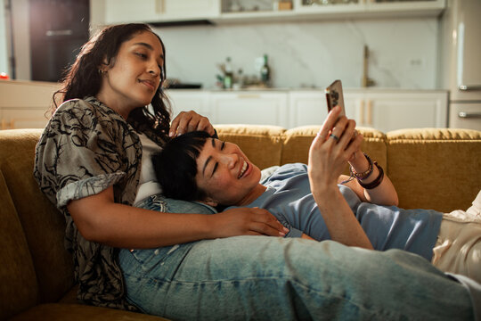 Two women relaxing on couch at home, looking at smartphone