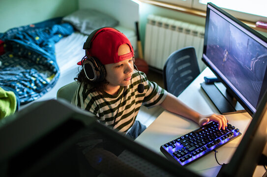 Teen gamer wearing headset playing pc game in bedroom at home