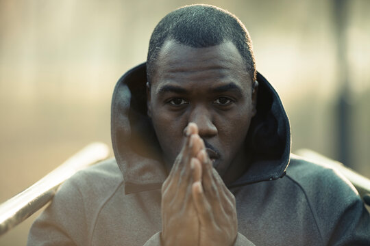 Focused man in hoodie with hands together outdoors at sunrise