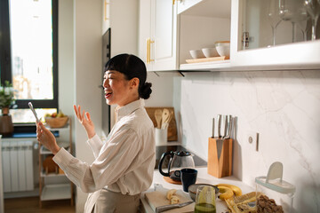 Smiling woman video calling while preparing breakfast in home kitchen