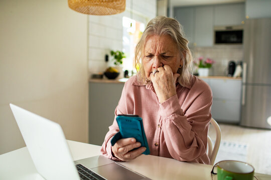 Senior woman worriedly checking smartphone at kitchen table at home