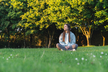 Serene young woman meditating in a lush green park, enjoying the tranquility of nature at sunset © Araguatai