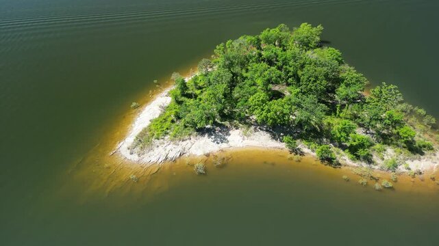 Drone video of forested island with dense trees and shoreline untouched nature summer scenery slowly flying sideway above water