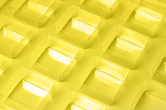 An industrial transparent square thermoforming mold made of plastic as a packaging solution for industrial products. Foil cubes on a white background and shining lights.