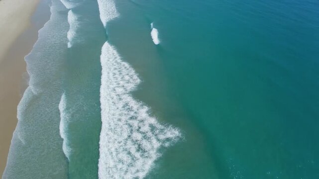 Aerial view of ocean waves crashing on sandy shoreline