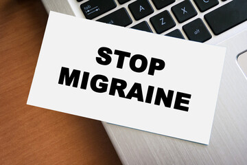 Handwritten note displaying the words STOP MIGRAINE on a white paper placed on a laptop keyboard. This image symbolizes health awareness and pain management strategies.