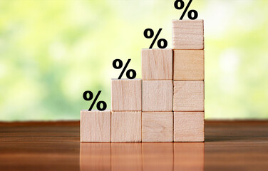 An arrangement of wooden blocks stacked in increasing order, each marked with percentage signs, symbolizing growth and progress in business metrics, set against a blurred green background.
