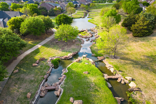 Aerial view of park waterway winding through green space with trees grass and pedestrian paths