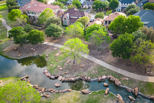 Aerial view of suburban park with creek trees lawns and walking paths near residential neighborhood