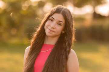 beautiful teenage brunette girl with long hair, smiling, looking at the camera during a summer walk