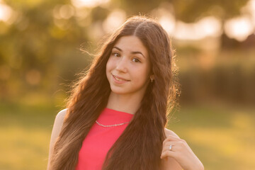 beautiful teenage brunette girl with long hair, smiling, looking at the camera during a summer walk