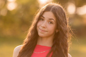 beautiful teenage brunette girl with long hair, smiling, looking at the camera during a summer walk