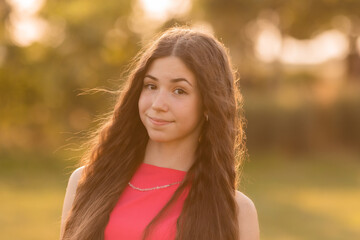 beautiful teenage brunette girl with long hair, smiling, looking at the camera during a summer walk