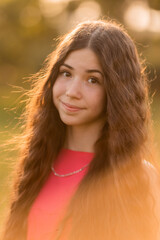 beautiful teenage brunette girl with long hair, smiling, looking at the camera during a summer walk