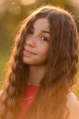 beautiful teenage brunette girl with long hair, smiling, looking at the camera during a summer walk