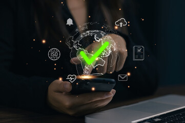 Business professional holding smartphone with global checkmark and compliance icons, representing ISO certification, global standard approval, quality assurance, and digital verification system.