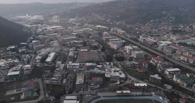 Aerial view of tanning factory buildings, roads, and a stadium, revealing a dense cityscape contrasting with rolling hills and mountains, Solofra, Campania, Italy.