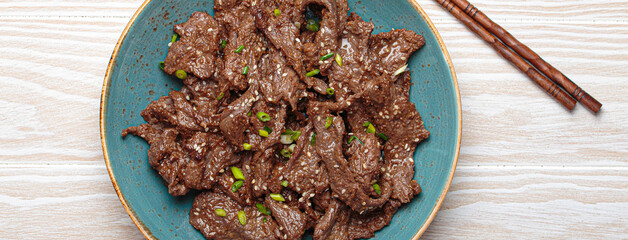 Delicious bulgogi dish served on plate on white wooden background top view, Korean cuisine