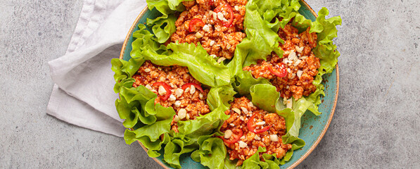 Lettuce wraps filled with minced meat and topped with peanuts and chili pepper flakes on a plate