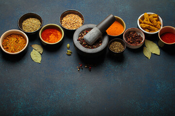 Mortar and pestle surrounded by colorful spices on dark background with copy space