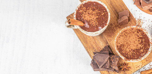 Hot chocolate cups with cocoa powder and cinnamon on wooden board, top view with copy space