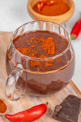 Spicy hot chocolate with chili pepper and cocoa powder in glass mug on wooden board