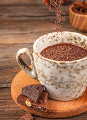 Hot chocolate with falling chocolate shavings in ceramic cup on wooden background