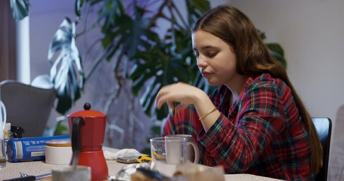 A young teenager enjoys a cup of coffee and a biscuit at the kitchen table in the morning.