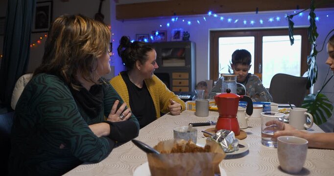 The family are sitting around the table, analysing each other's gestures in order to identify the imposter in the digital game, while enjoying coffee and cake.