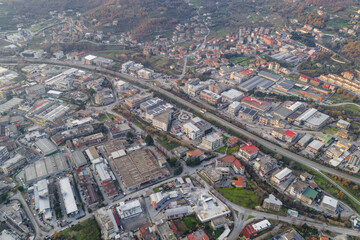 Aerial view of a road slicing through a landscape of factories and tanning factory buildings, contrasting with the backdrop of rolling hills, Solofra, Campania, Italy.