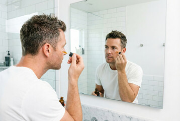 Man applying skincare product in front of a bathroom mirror, showcasing morning routine, grooming, clean, hygiene, reflection
