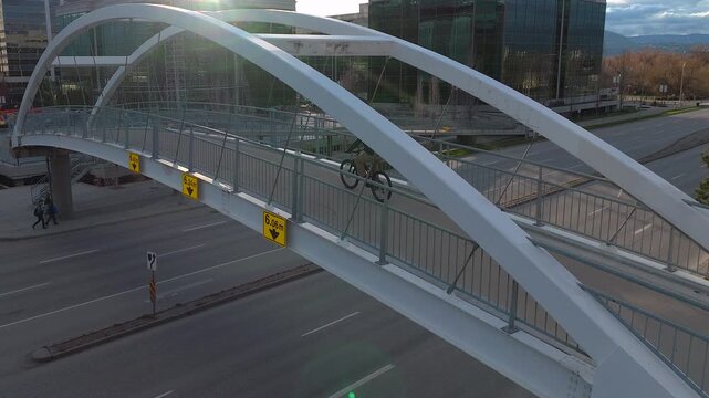 Man rides bike on an arched pedestrian overpass over a large multi lane city highway on a sunny day
