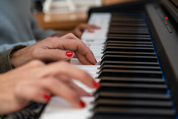 Obraz premium Two sets of hands with red nail polish pressing black and white piano keys, creating music. Learning and practicing