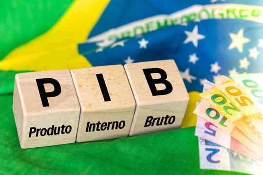 The word PIB, Produto Interno Bruto (Gross Domestic Product) written on wooden cubes with Brazilian real money in yellow, green flag of Brazil. Brazilian Portuguese language