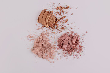 Three crushed and broken piles of brown, gold, bronze eye shadows on a pastel background. A sample texture of decorative cosmetics. top view.