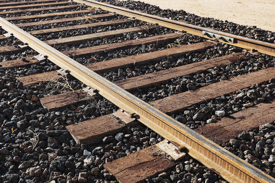 Railway track closeup detail. Steel rail and wooden sleepers. Gravel ballast texture background. Industrial transport infrastructure surface. Old railroad line perspective. Freight train route concept