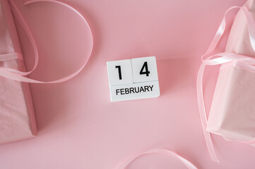 Top view of February 14 wooden calendar blocks on pink background with gift boxes and ribbons. Valentine's Day flat lay concept.