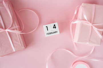 Top view of February 14 wooden calendar blocks on pink background with gift boxes and ribbons. Valentine's Day flat lay concept.